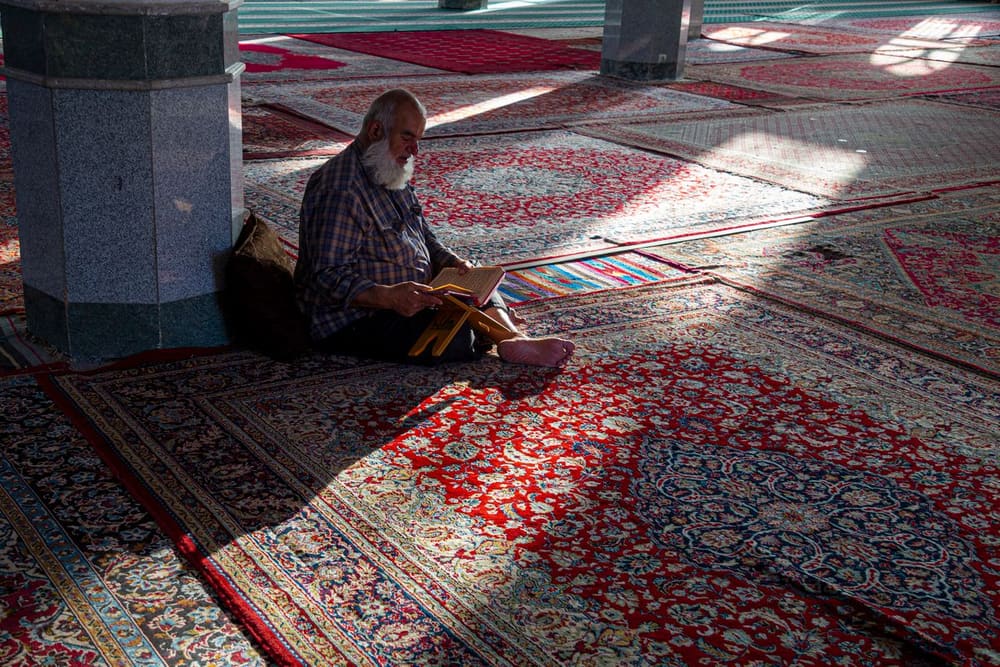 An elderly man reading the Qur'an in a mosque