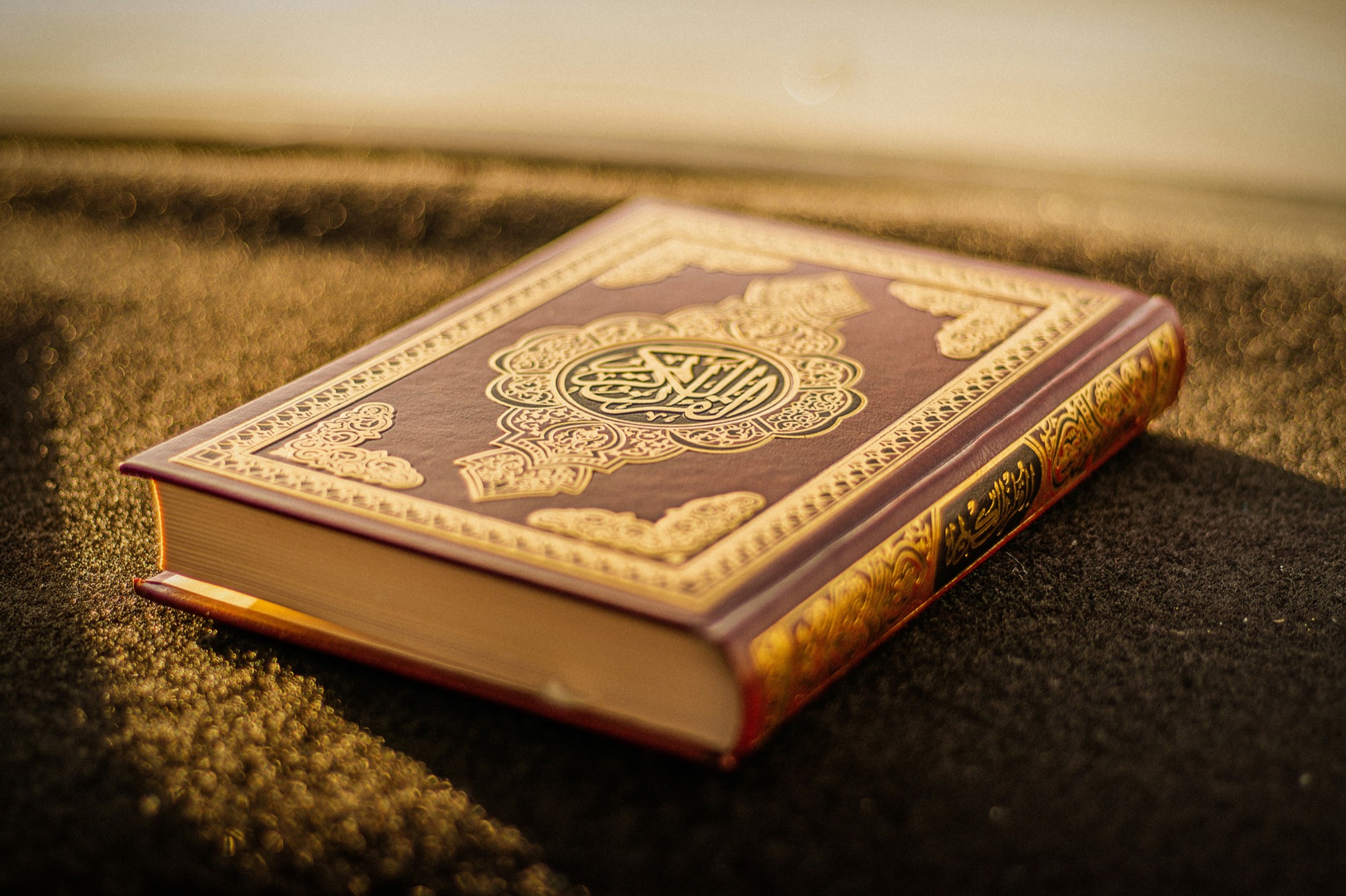 A closed mushaf with gold-embossed cover lit by warm low sunlight