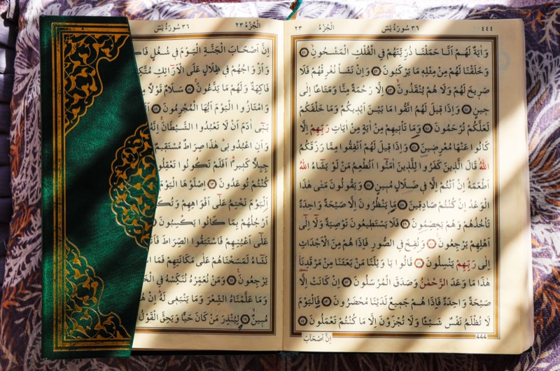 An open Qur'an showing Surah Ya-Sin, lit by shafts of sunlight