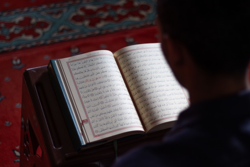 A young man reading from a Qur'an on a wooden rehal in a mosque