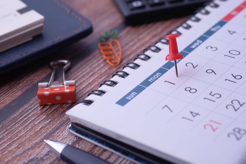 A desk calendar marked with a red pin beside a notebook and pen