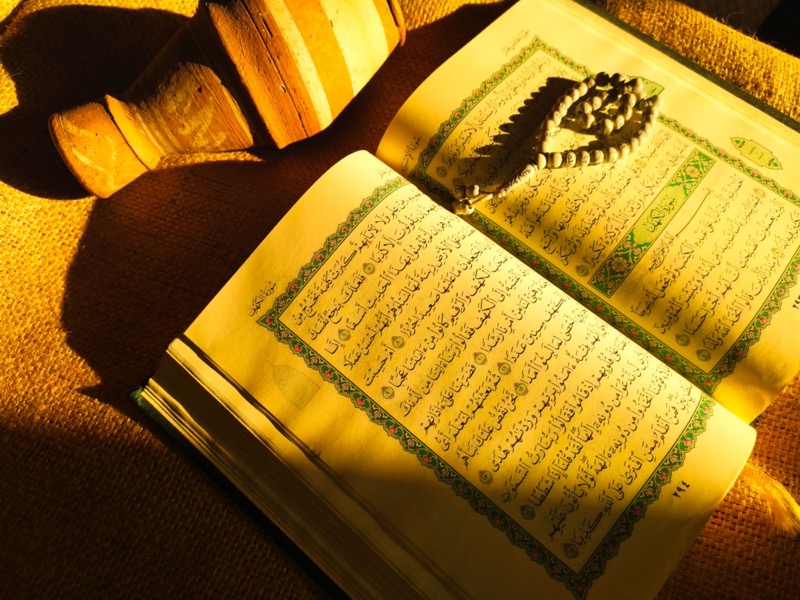 An illuminated Qur'an open beside prayer beads in warm golden light