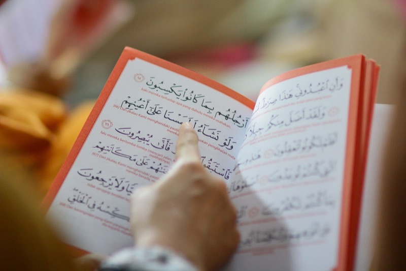 A reader following the lines of a Qur'an with translation beneath the Arabic