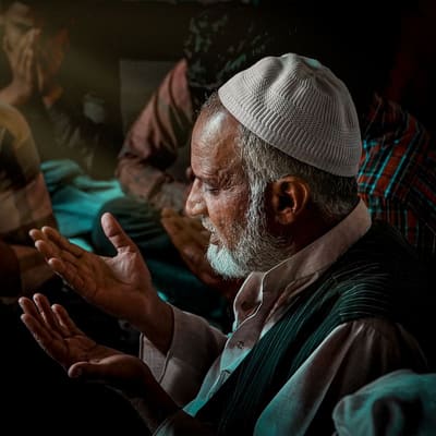 Open hands raised in dua beside an open Qur'an