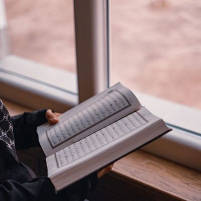 A person quietly reciting the Qur'an in the calm light of early morning