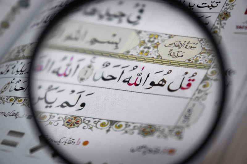 A magnifying glass held over a page of the Qur'an, enlarging the Arabic text