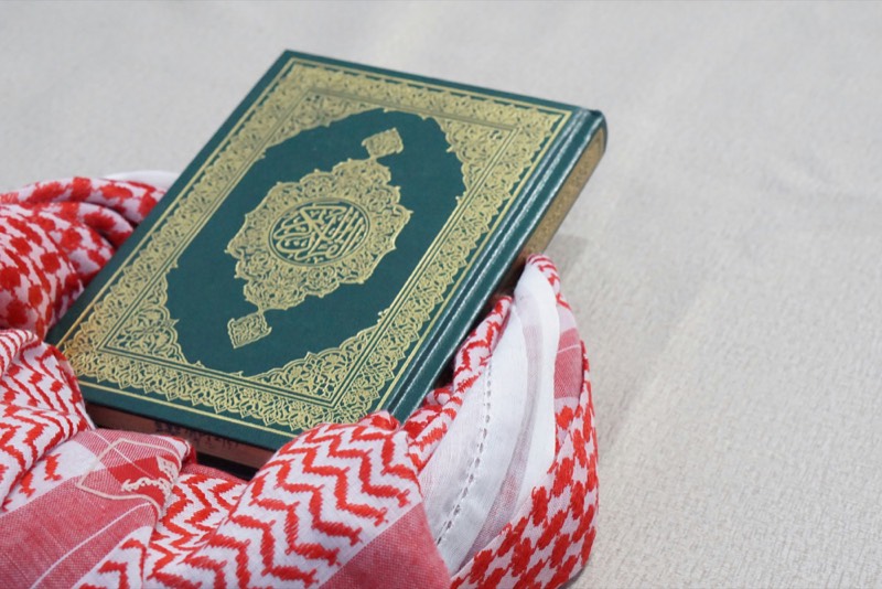 A green and gold mushaf resting on a folded red and white keffiyeh