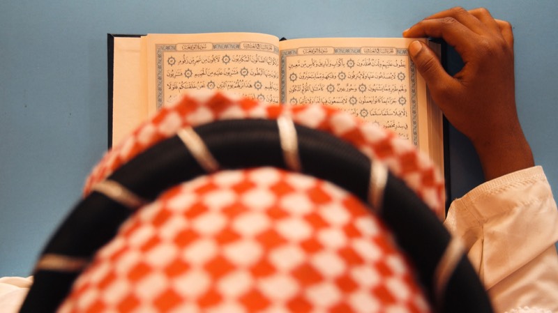 Overhead view of a man in a patterned keffiyeh revising from an open mushaf